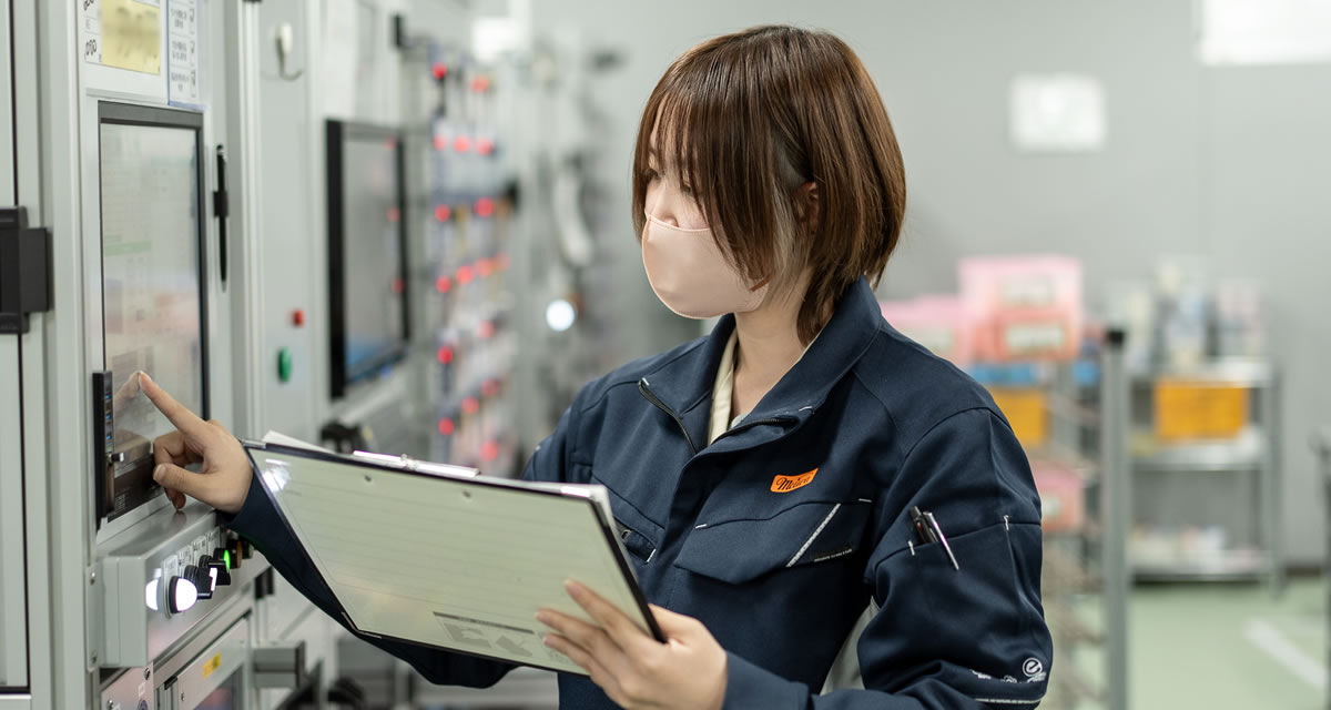 工場で設備の操作盤を確認する女性作業員