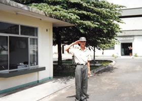 工場敷地内で敬礼する作業服の男性